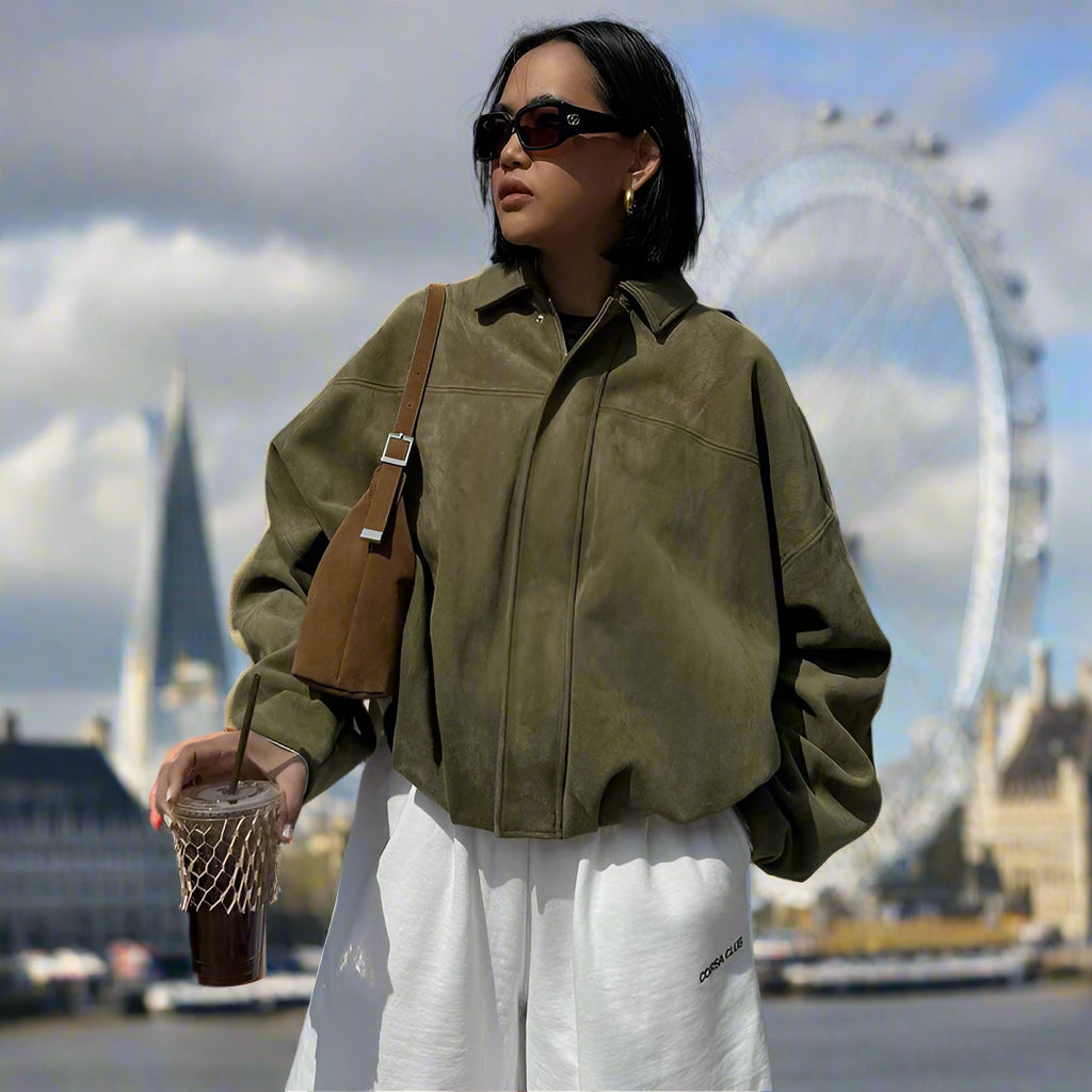 Woman in a green jacket and white pants standing on a rooftop with a cityscape background