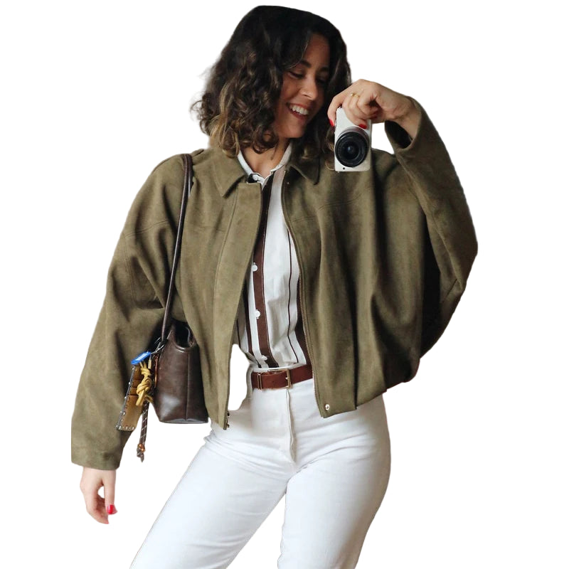 Woman taking a selfie wearing an olive green jacket and white pants in a living room.